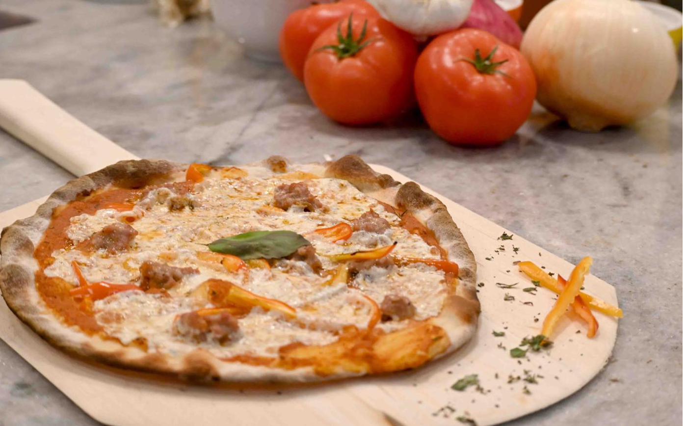 Wood-fired pizza topped with mushrooms, fresh spinach, and melted mozzarella on the pizza stone